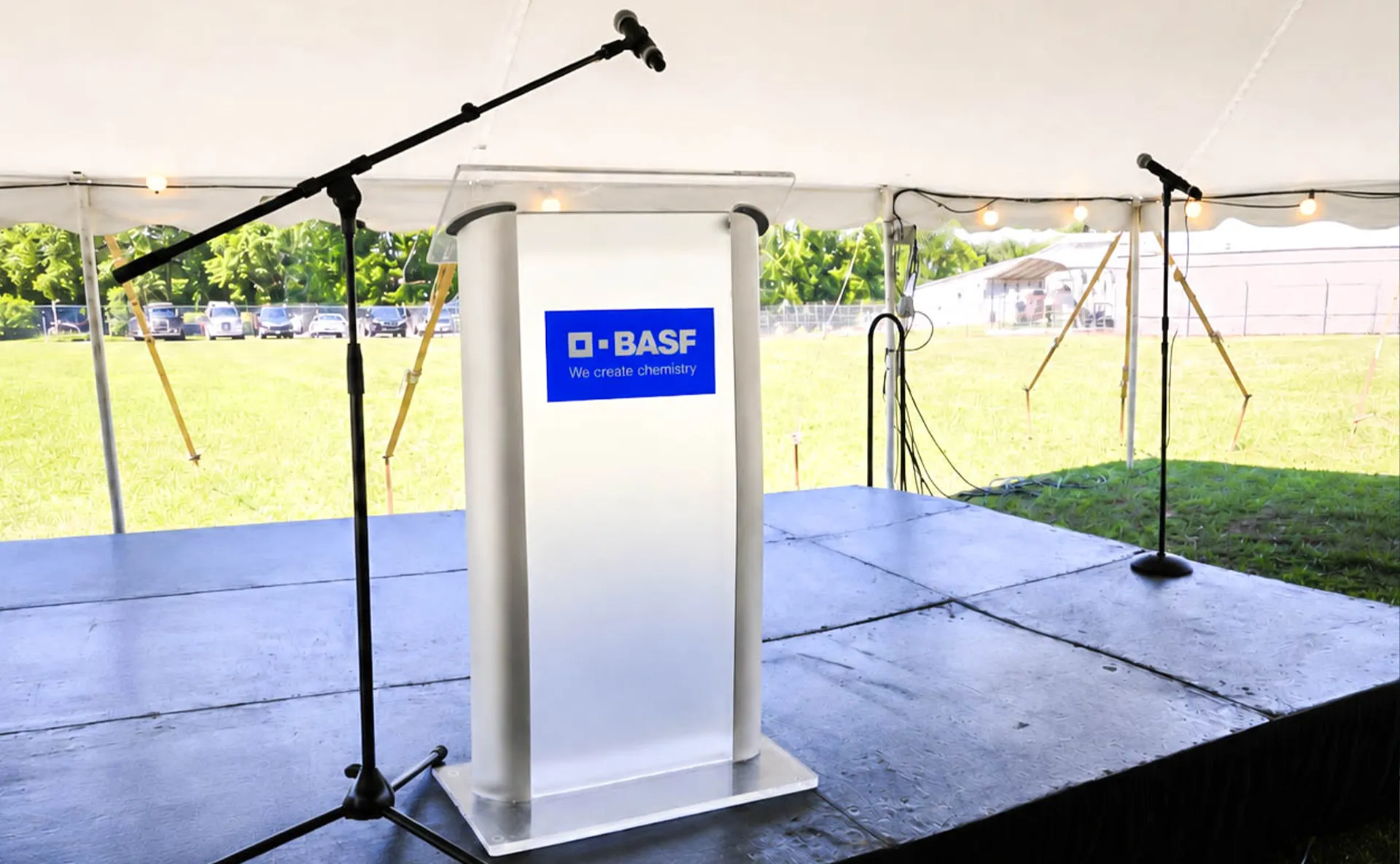 Outdoor corporate event production stage with BASF-branded podium, microphones, and presentation setup under a tent