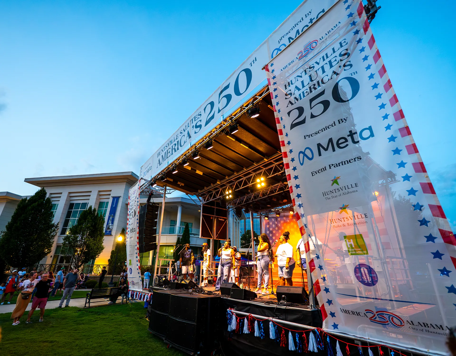 Performers on an outdoor live event stage with concert lighting at Huntsville Celebrates America's 250th in downtown Huntsville.